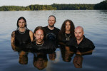 HammerFall-bändin jäsenet seisovat olkapäitä myöten vedessä, järvessä. Taustalla kuusimetsää ja sinistä taivasta.