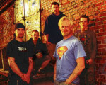 sinKing-bändin promokuva, jossa viisi miestä seisoo punatiilikiviseinää vasten. Yhdellä miehistä on Superman-paita.