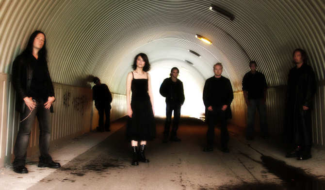 Silentiumin seitsenhenkinen joukkue poseeraa suuren tunnelin suuaukolla. Taustalla tunnelin toisessa päässä valkoisena hohtavaa valoa. Kuvassa näkyy kuusi miestä ja heidän keskellään mustahiuksinen ja mustiin pukeutunut nainen.