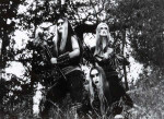 Astarte-bändin jäsenet, eli kolme naista, seisovat keskellä korpea mustavalkoisessa kuvassa. Naisilla corpse-paintit kasvoilla.