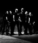 Chimaira-bändin jäsenet seisovat mustavalkoisessa valokuvassa rivissä, mustiin vaatteisiin pukeutuneena. Kuvakulma on ruohonjuuritasolta.