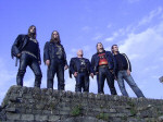 Emerald-bändin jäsenet seisovat rivissä muurinharjalla sinisen taivaan alla.