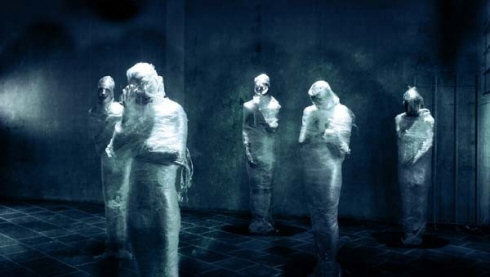 Compos Mentis -bändin jäsenet seisovat kylmänsinisessä valokuvassa käärittyinä muoviin. Miehet näyttävät muumioilta. Muovi saattaa olla Elmu-Kelmua. Yksi miehistä vilkuttaa...