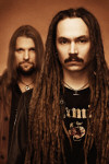Amorphis-bändin kaksi jäsentä ruskeasävyisessä kuvassa. Kummallakin miehellä on viikset, taaemmalla myös partaa. Miehillä pitkät hiukset, etualalla näkyvän miehen hiukset on laitettu rastoiksi.