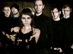 Deadlock-yhtyeen jäsenet seisovat rivissä. Kuvan etualalla näkyy nainen, jolla on kädet ojossa. Taaempana näkyy viisi miestä, joilla kaikilla mustat vaatteet yllään.