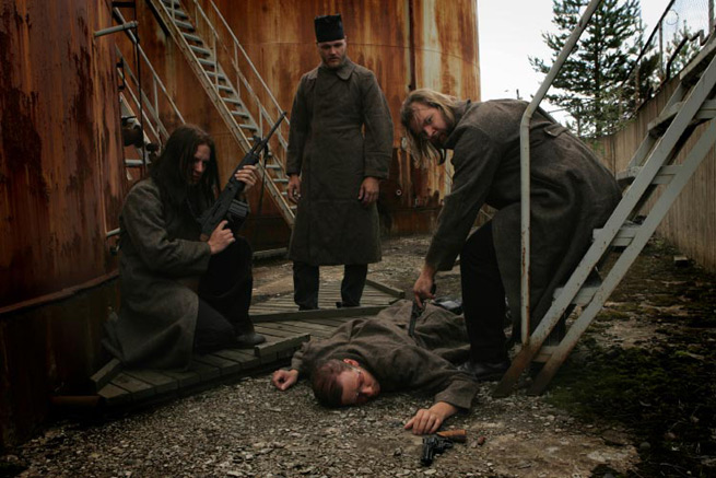 Promokuva doom metal -bändi KYPCK:in kokoonpanosta, johon kuuluvat jäsenet ovat miehiä ja pukeutuneet harmaista ja mustista kankaista valmistettuihin vaatteisiin. Miehet ovat kerääntyneet maassa makaavan henkilön ympärille.