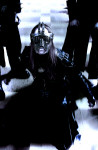 Behemoth-yhtyeen keulahahmo kyyristelee kahden miehen tummien hahmojen edessä. Miehellä on päässään kiiltävästä metallista rakennettu kasvokypärä ja päällään mustat nahkavaatteet.