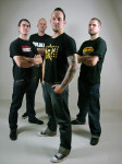 Volbeat-bändin neljä jäsentä seisovat valkoista taustaa vasten. Miehillä yllään t-paidat ja farkut. Paidoissa on tekstiä ja logoja. Jokaisella miehellä lyhyet hiukset.