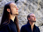 Dornenreich-yhtyeen kaksipäinen miehistö, joista molemmat ovat miehiä, seisovat kallioseinän edessä. Miehillä on yllään samanlaiset tummansiniset paidat ja pitkät hiukset, sekä leukaparta. Miehet katsovat oikealle ylöspäin.