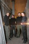 Faerghail-bändin jäsenet seisovat kuvassa varastotiloissa, kummassakin laidasssa kanaverkkoaitaa. Kuvassa neljä miestä, jotka seisovat puoliympyrämuodostelmassa ja katsovat eteenpäin.
