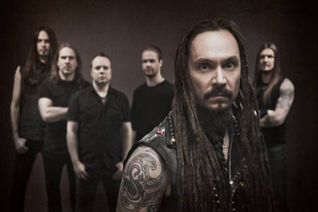 Kuvassa Amorphis ja etualalla bändin vokalisti Tomi Joutsen. Yhtyeeltä ilmestyy huhtikuussa uusi studioalbumi. Ryhmäkuva Amorphiksen kokoonpanosta seisomassa tummanruskeaa taustaa. Etualalla viiksekäs ja rastapäinen Tomi Joutsen.